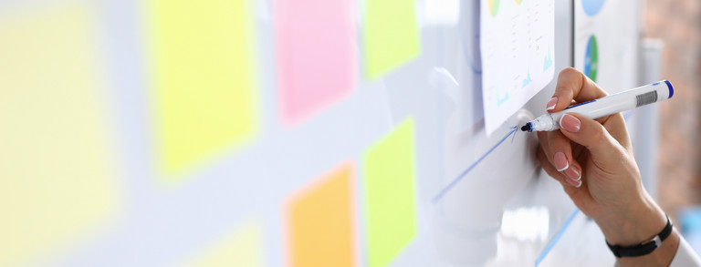 Frau zeichnet Pfeil auf Whiteboard, auf dem bunte Post-Its kleben