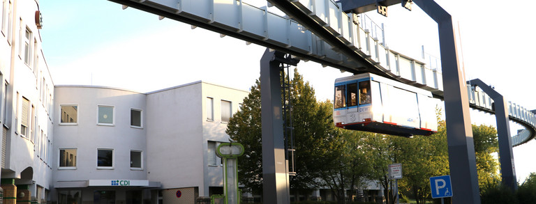 Foto von dem weißen CDI-Gebäude bei Sonnenuntergang mit vorbeifahrender Schwebebahn der TU Dortmund.