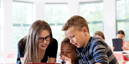 Foto einer Lehrkraft mit zwei Grundschulkindern am Laptop